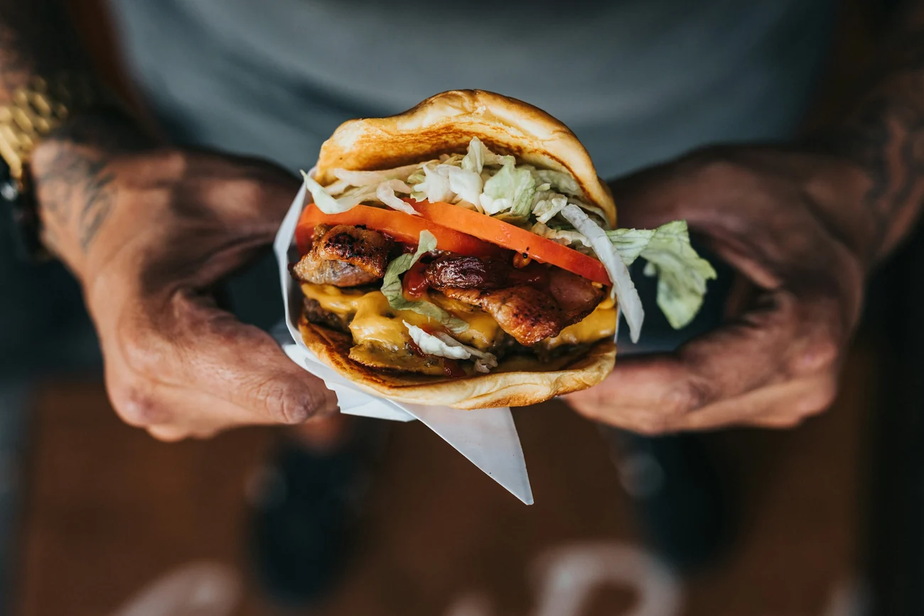 Two hands passing a wrapped smash burger across the counter